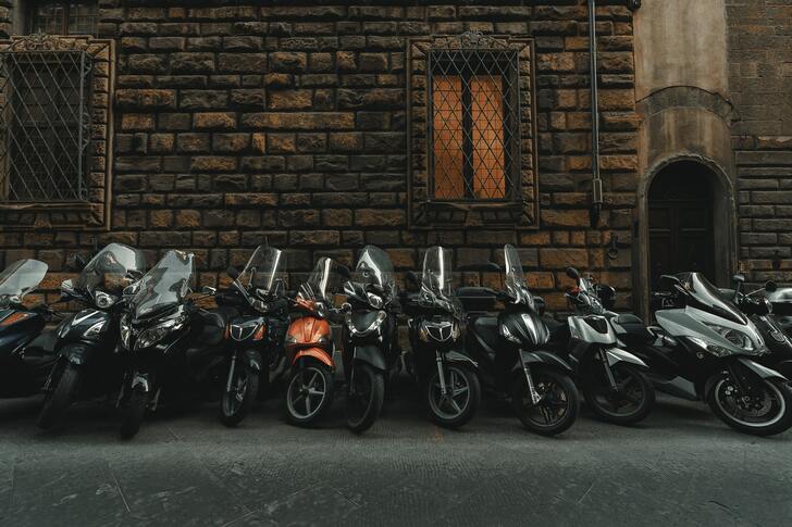 One orange moped between 10 black mopeds.